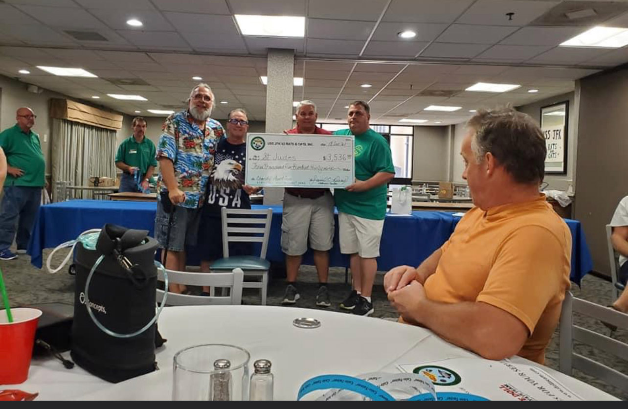 A group of men standing around at tables holding up a large check.