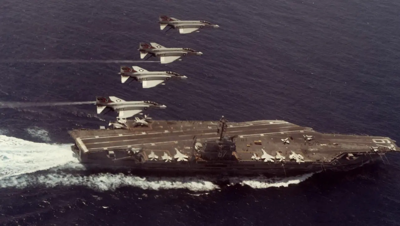 A group of jets flying over an aircraft carrier.